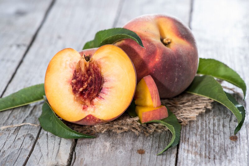 on a rustic wooden surface is a whole and a half peaches resting on top of a small piece of burlap with a few green leaves