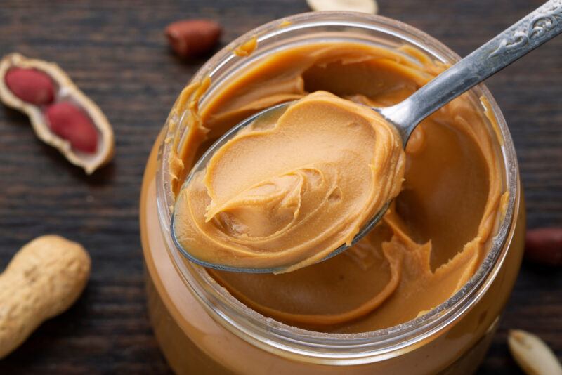 a closeup up top view shot of an open jar of peanut butter, with a spoonful of peanut butter, with loose peanuts around it