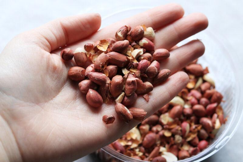 a hand full of peanuts held over a bowl with peanuts as well