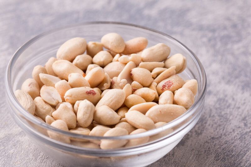 a clear glass bowl full of peanuts resting on a concrete surface