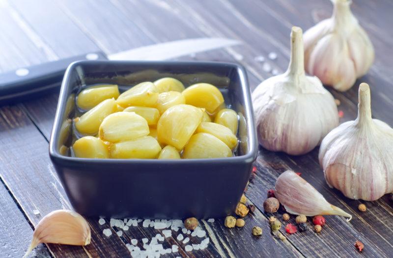 three heads of garlic, a paring knife and freshly-peeled garlic in a blue square bowl
