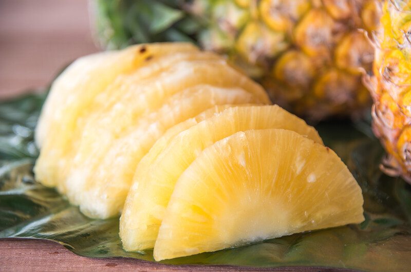 closeup image of slices of pineapple with whole pineapples at the back