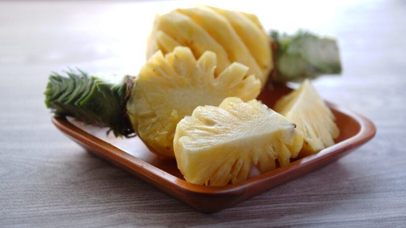 on a wooden surface is a square dish with peeled and cut pineapples