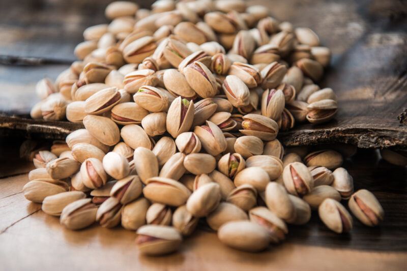 on a wooden surface is a wooden board with a pile of pistachios