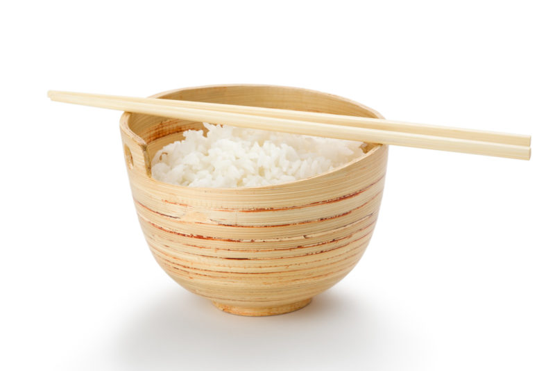 A wooden bowl filled with plain cooked rice, with a pair chopsticks resting on top of it