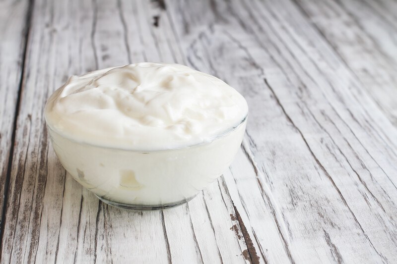 on an aged wooden surface is a clear glass bowl of plain yogurt