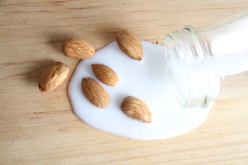 A bottle with milk spilling out of it into a small pile of almonds to represent plant based milk 