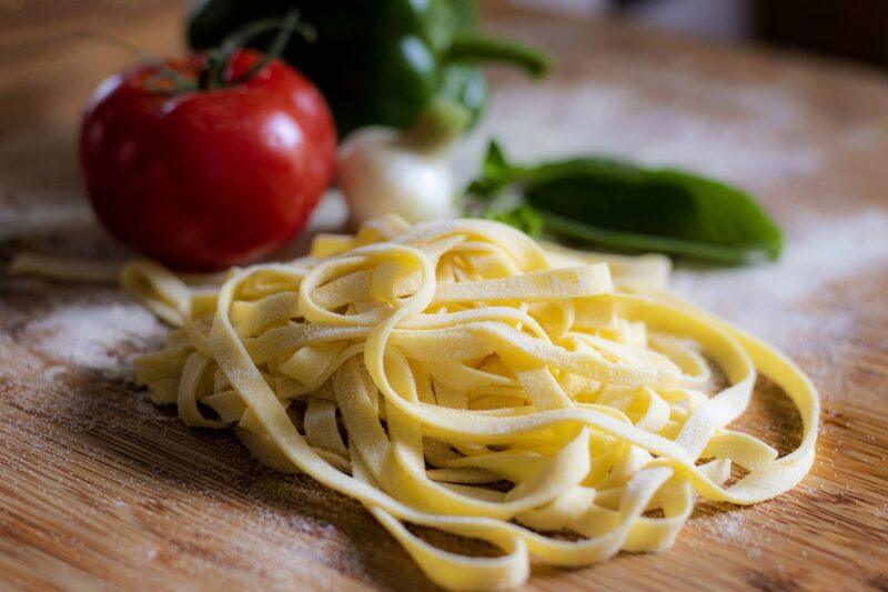 fresh pasta noodles with a tomato and pepper behind it to represent plant based pasta