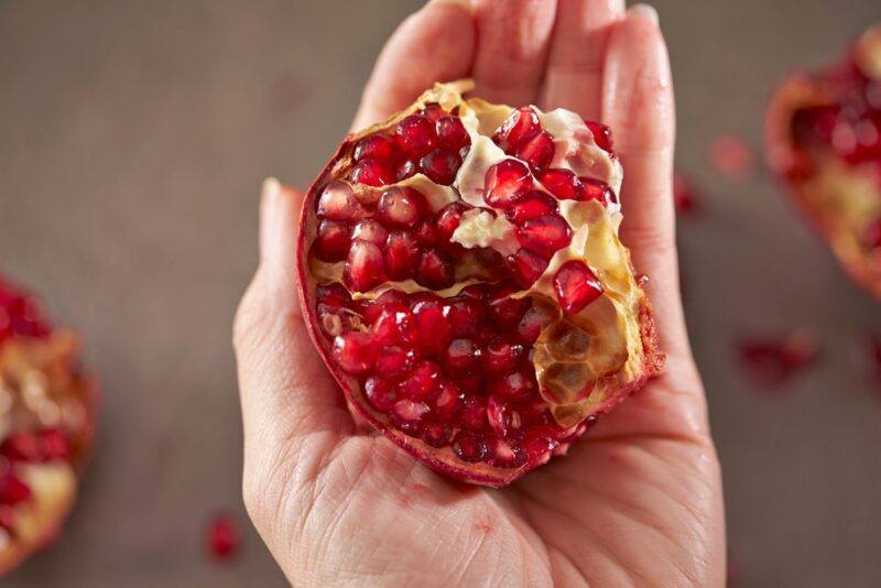 an open hand holding a piece of pomegranate