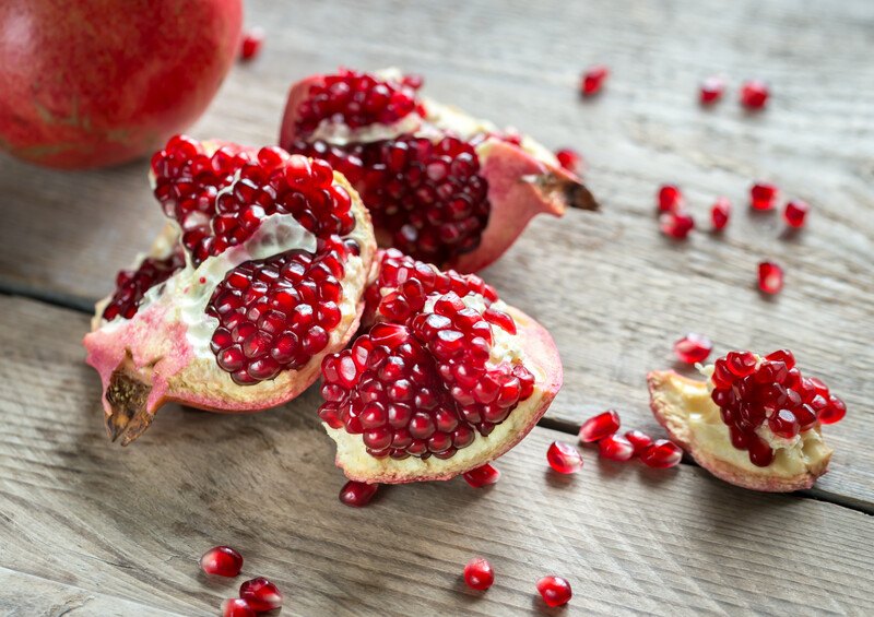 on a wooden surface is a closeup image of slices of pomegranate with seeds showing, some of the seeds are loosely scattered around it