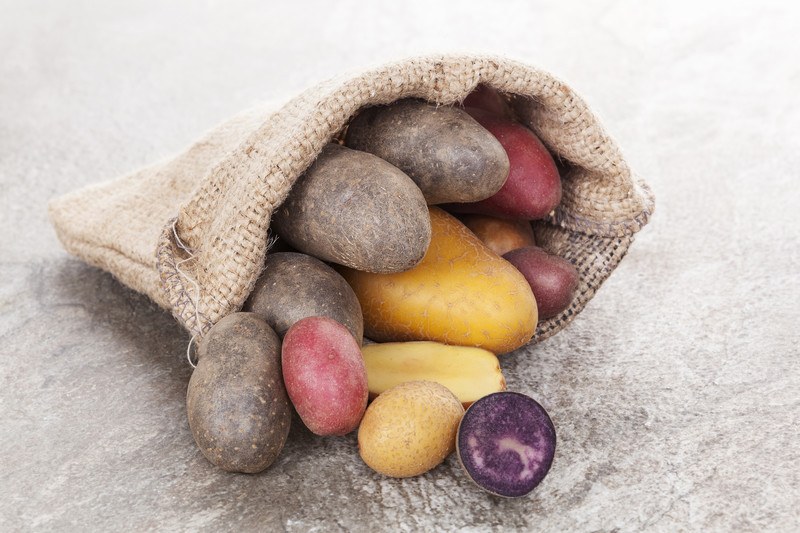 on a marbled surface is a closeup image of a burlap sack with different types of potatoes pouring out from it