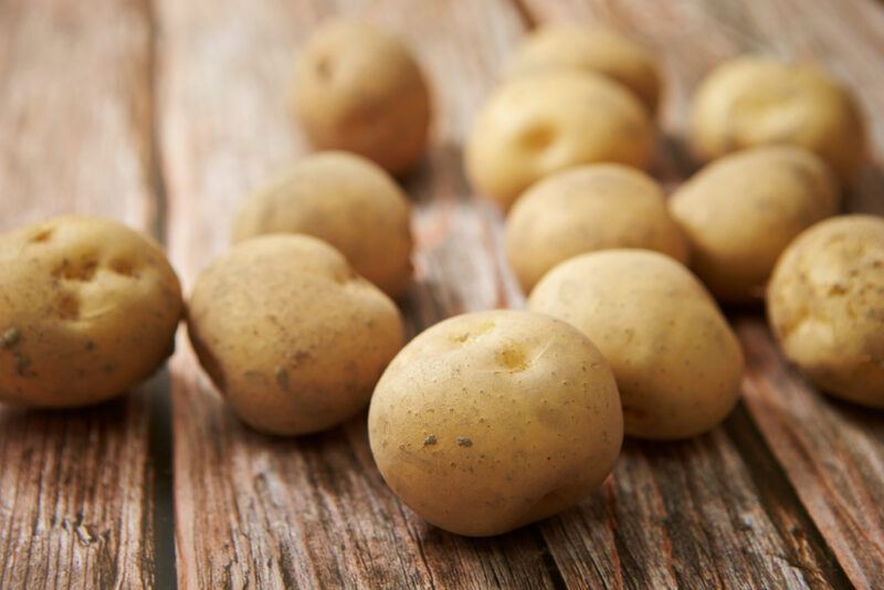 on a rustic looking wooden surface are fresh potatoes