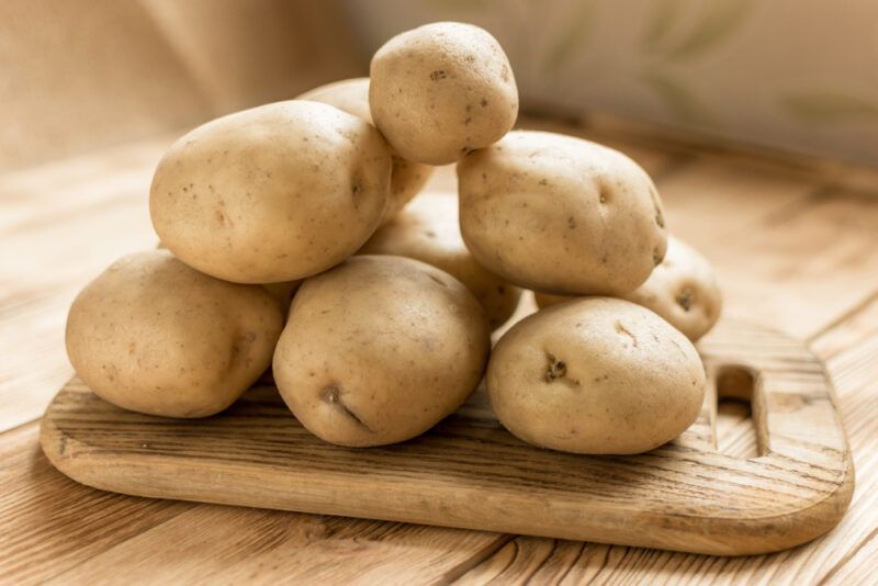 on a wooden surface is a wooden chopping board with a pile of potatoes