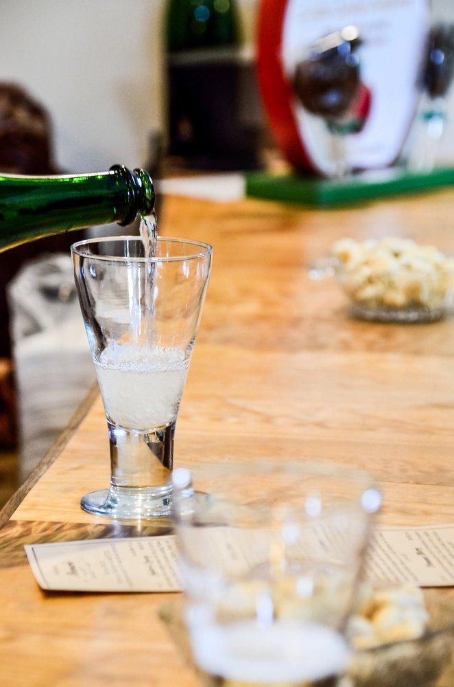 pouring glass of artisanal cider from green bottle in tasting room