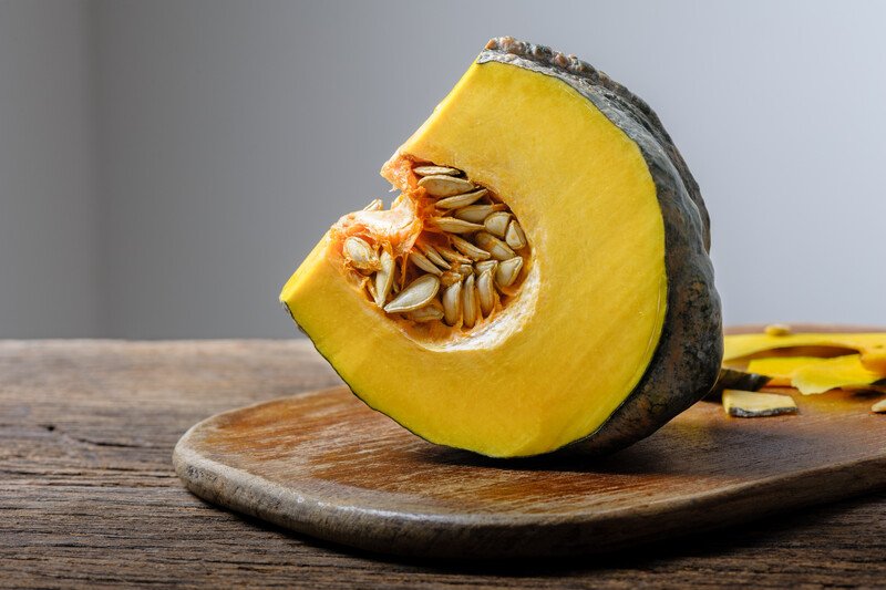 a big sliced of pumpkin with skin and seeds still on resting on a round wooden board