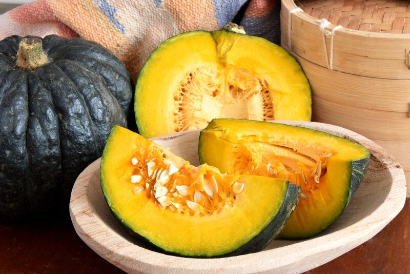 closeup image of cut pumpkin on a wooden dish with a whole pumpkin at the back