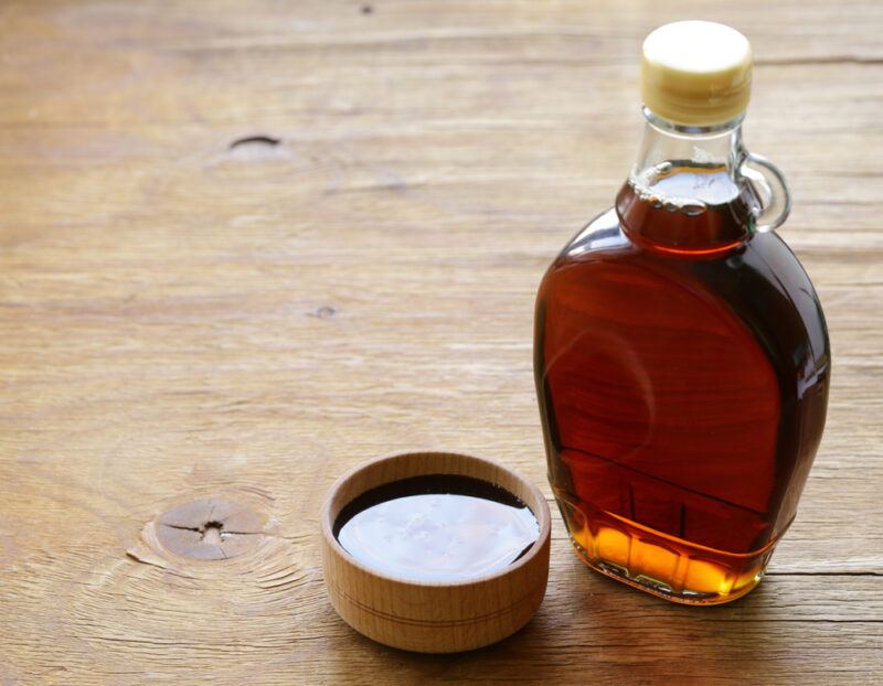 on a wooden surface is a bottle of pure maple syrup with a small wooden bowl beside it also with maple syrup