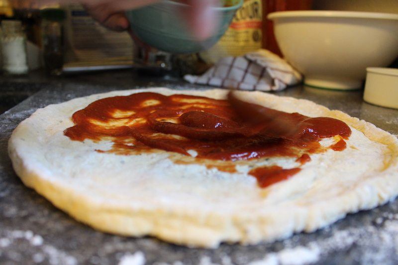 spreading homemade pizza sauce on homemade pizza dough for grilling outside