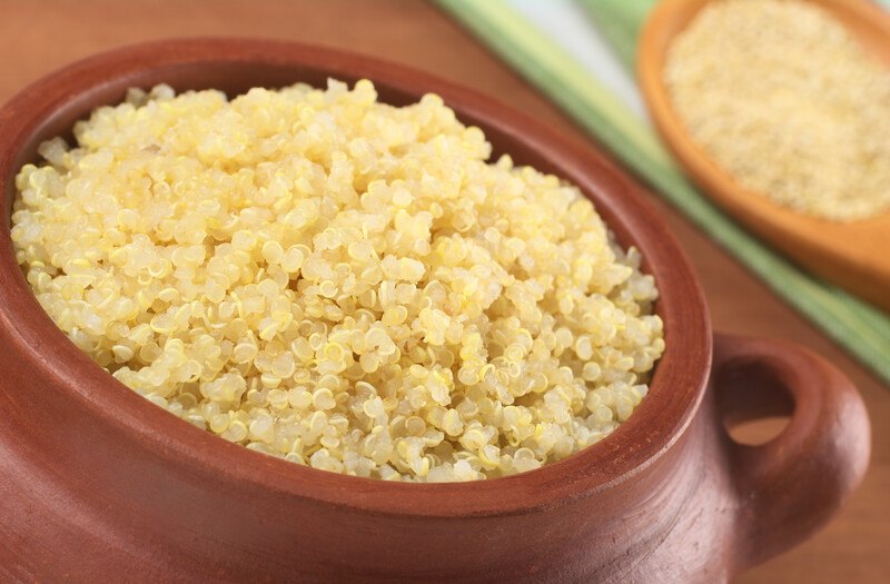 A brown bowl of cooked yellow quinoa rests on a wooden table.