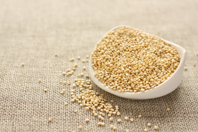 on a neatly laid out burlap is a white dish full of quinoa with loose quinoa around it