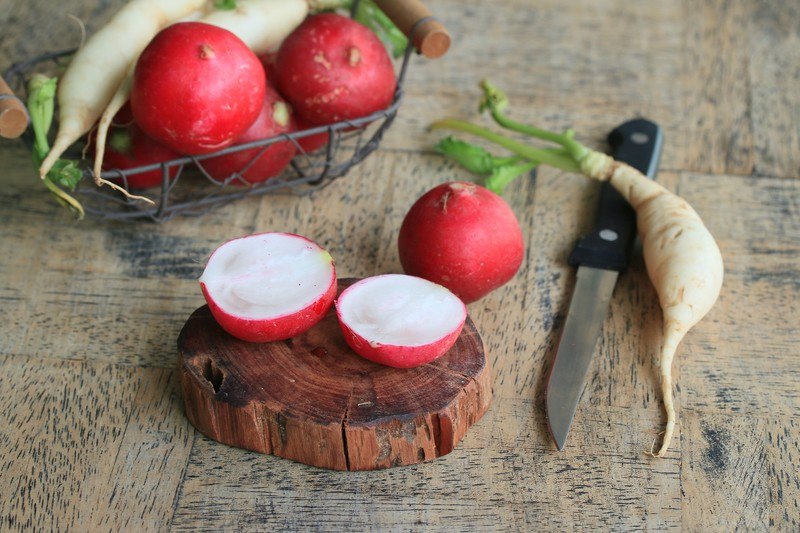 red and white radishes, with a knife and small round chopping board with halved pink radish