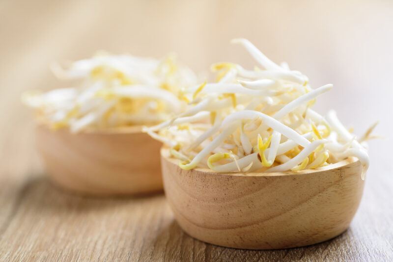 on a wooden surface is a couple of wooden bowls full of raw bean sprouts