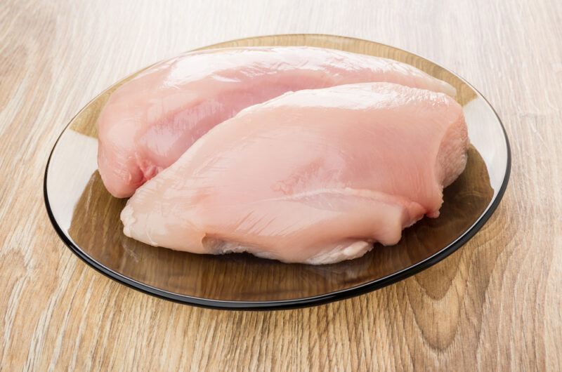 on a wooden surface is a glass brown plate with a couple of raw chicken breast