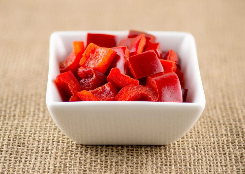 on a brown table cloth is a square white dish full of diced red bell pepper