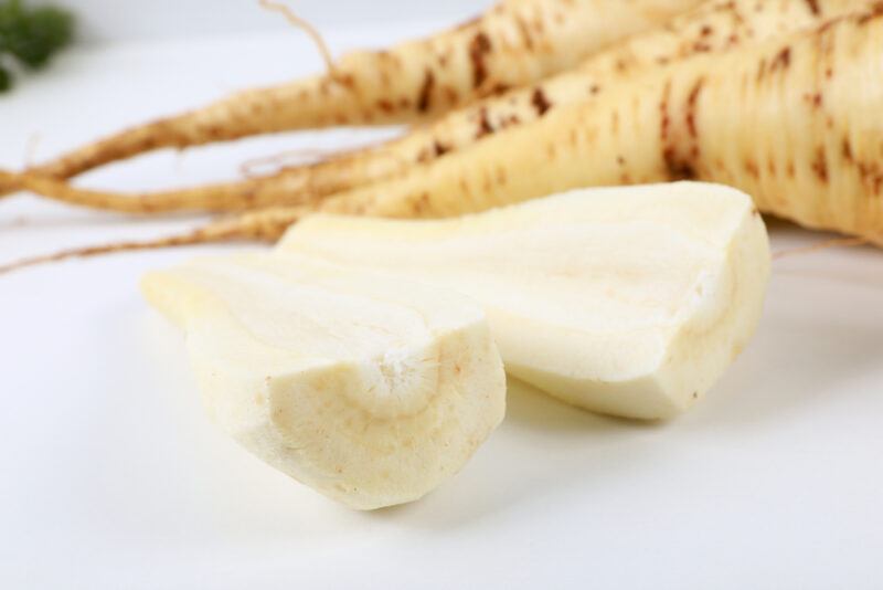 on a white surface are raw parsnips with the one at the foreground peeled and halved