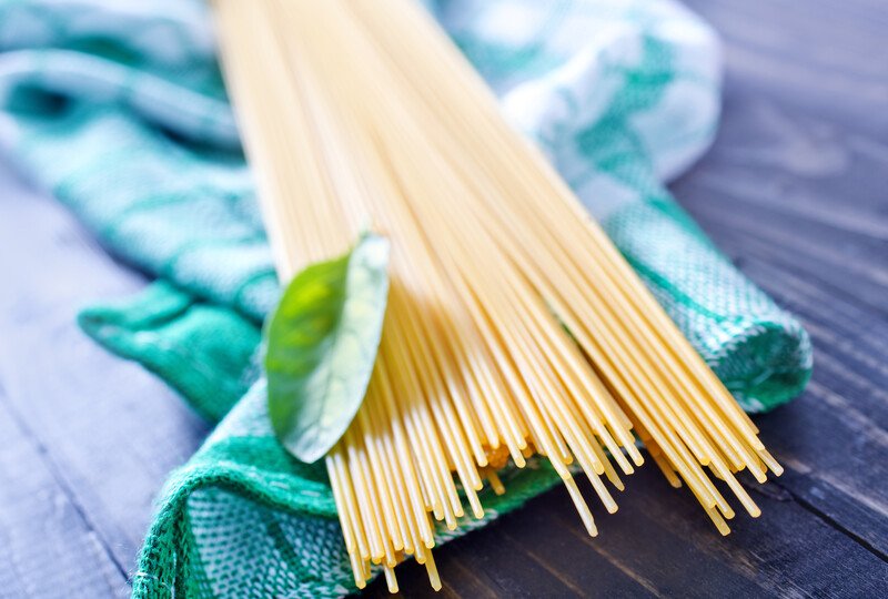 a closeup image of raw white pasta resting on top of a white and green table napkin, there is also a single herb on top of the pasta