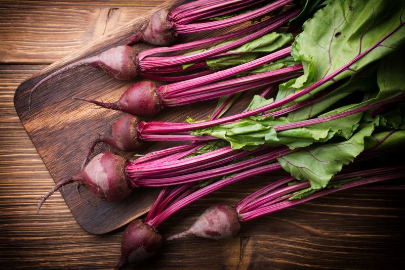 red beets with their stems on a wooden chopping board