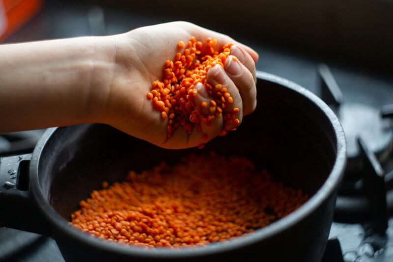 hand holding a handful of red lentils over a pot also with red lentils 