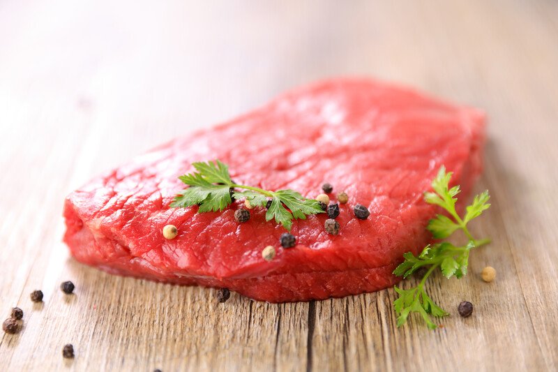 red meat | Food For Net on a wooden surface is a big piece of red meat with herbs and spices on top and around it