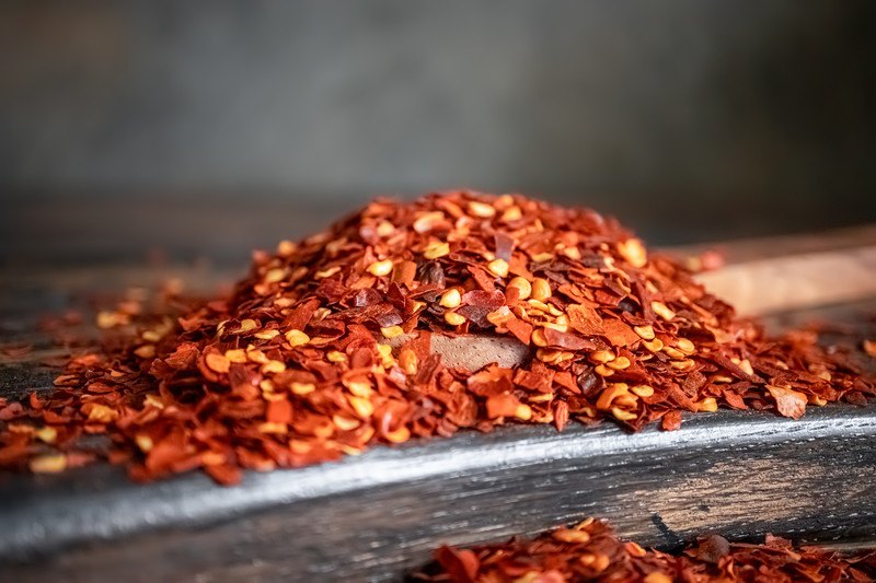 closeup image of a black wooden surface with a mound of red pepper flakes