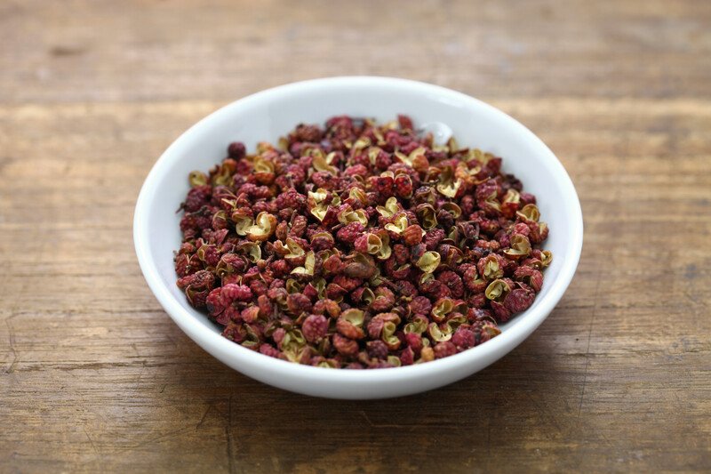 wooden surface with white bowl full of red sichuan peppers