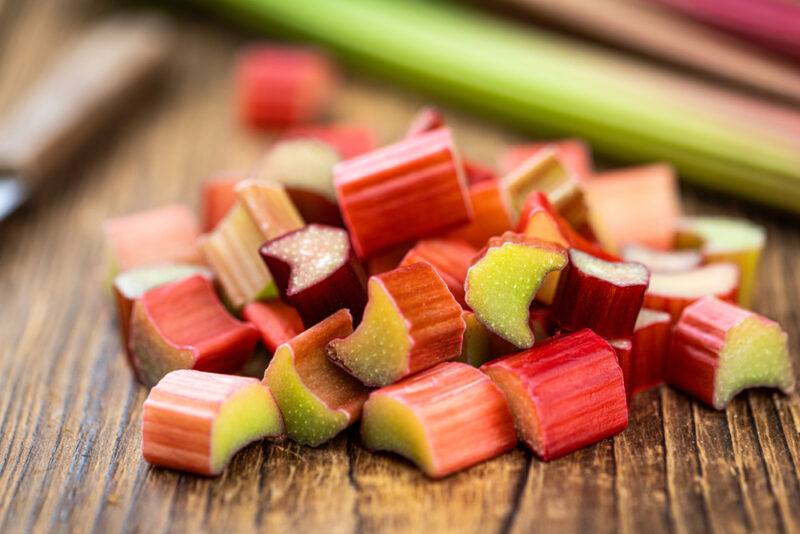 on a wooden surface are chopped rhubarbs with whole rhubarbs and knife at the back