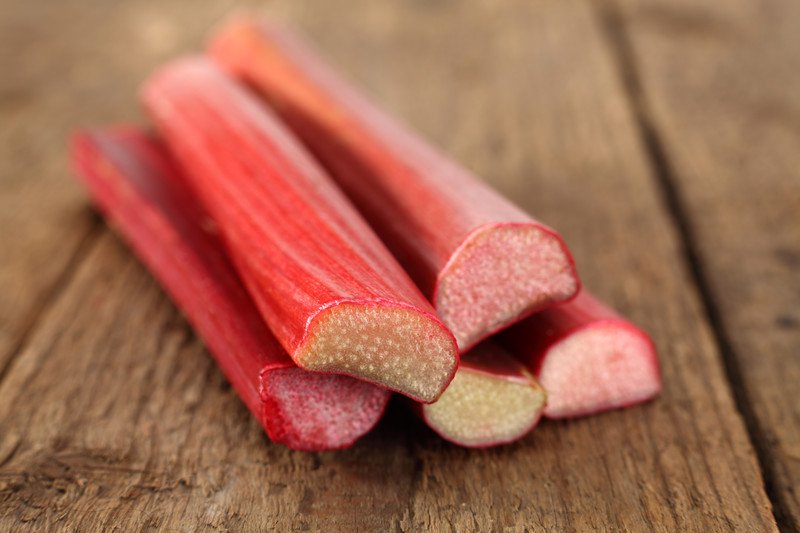 rhubarb | Food For Net Five stalks of red rhubarb rest on a wooden tabletop.