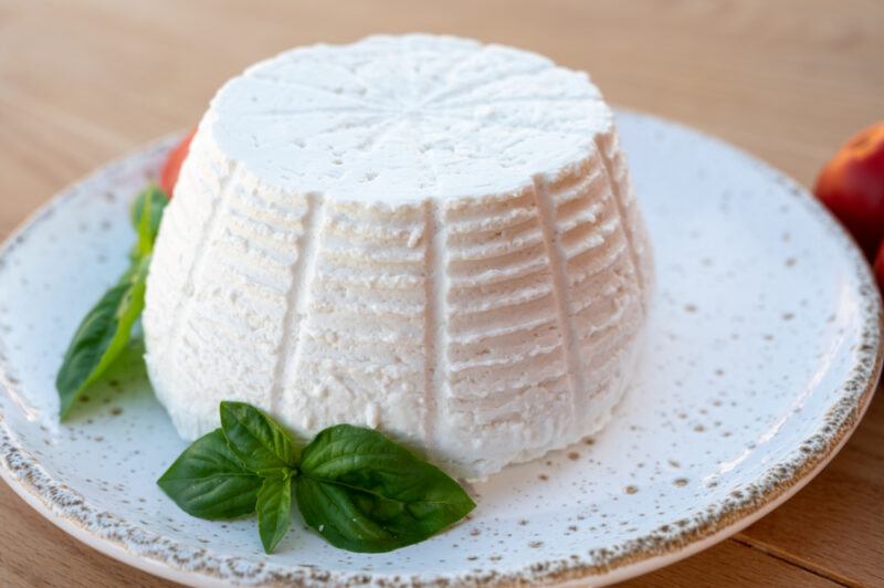 on a wooden surface is a white dish with fresh ricotta cheese with a couple of sprigs of mint