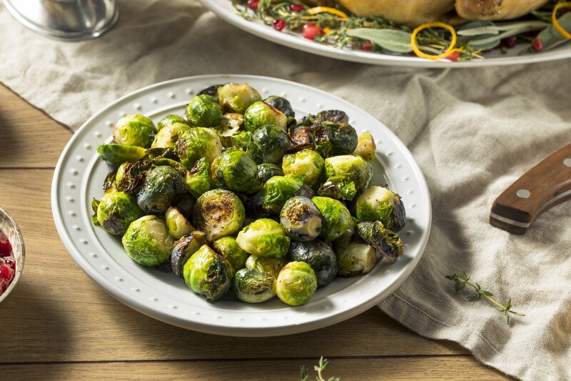 white dish with roasted brussels sprouts with table napkin underneath