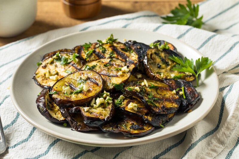 white dish with roasted sliced eggplants with herbs, underneath is a striped white and green table napkin