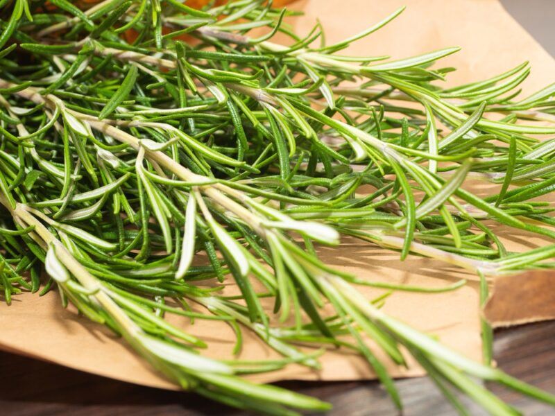 a closeup image of a sprigs of fresh rosemary resting on a round wooden chopping board