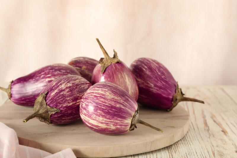 on a wooden surface is a wooden round chopping board with round eggplants on it