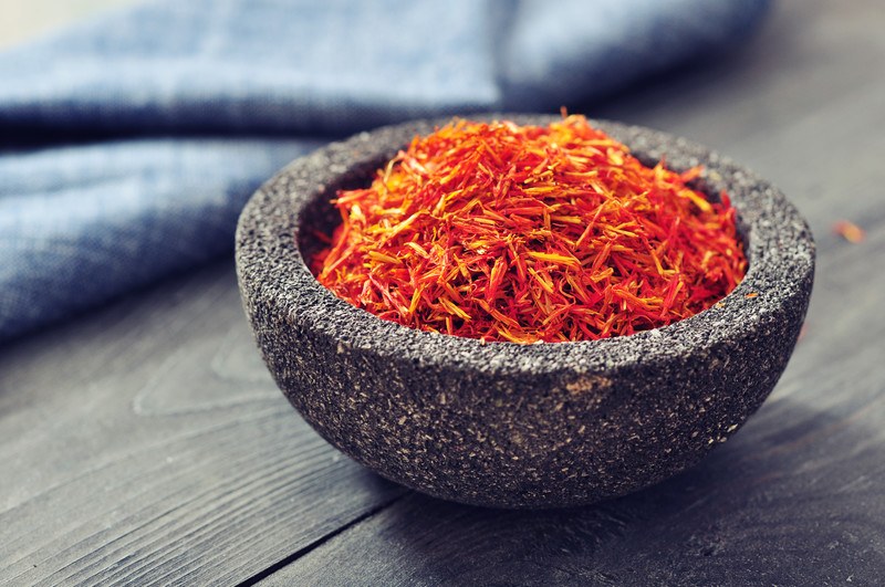 saffron threads in a stone bowl resting on a wooden surface with a blue table napkin at the back