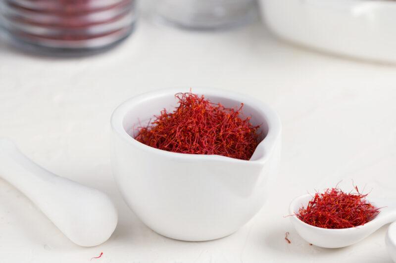 on a white surface is a small white jar with saffron, a small white saucer with saffron as well and a white ceramic spoon