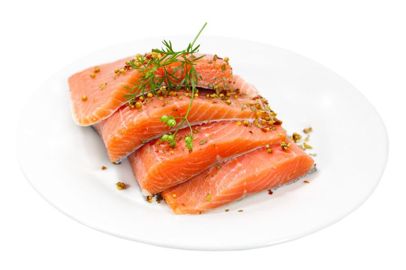 This photo shows a white plate with four slices of raw salmon and a green leaf garnish, against a white background.