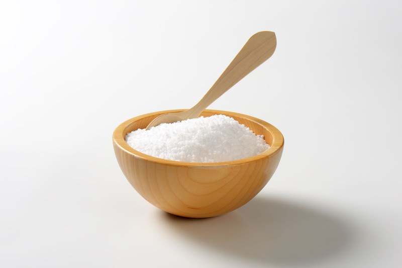 A wooden bowl of salt with a wooden spoon rests on a white tabletop.