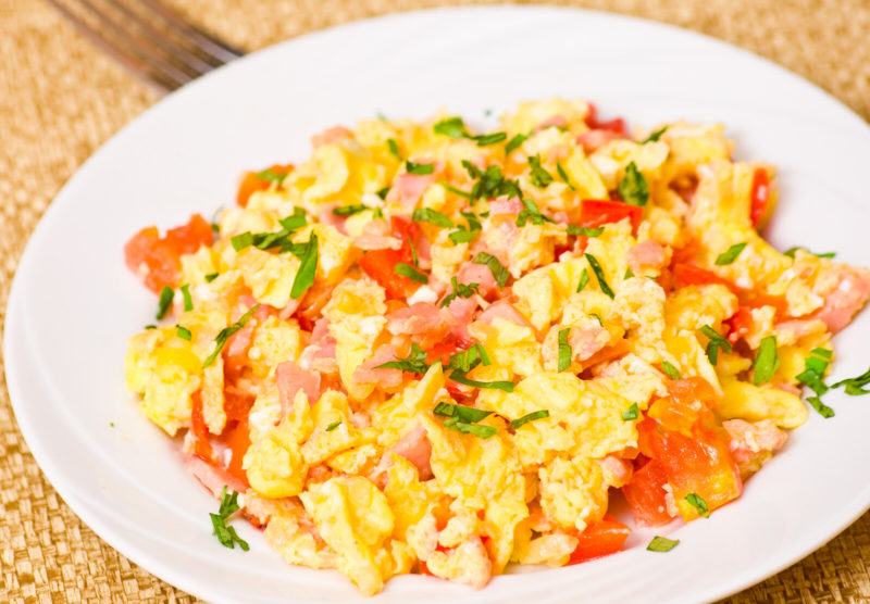 scrambled eggs with basil, tomatoes, and ham on a white plate