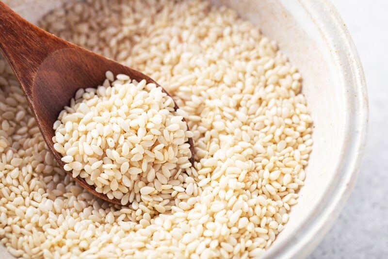 on a white surface is a white bowl of white sesame seeds with a wooden spoon shoved in it