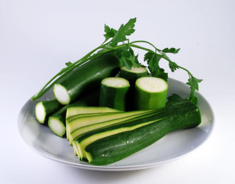 whole cucumbers with ends cut off, plus one cucumber sliced lengthwise on a white plate