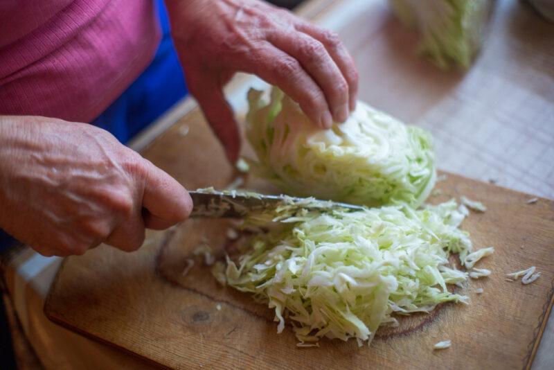 partial image of hands shredding cabbage on a wooden chopping board